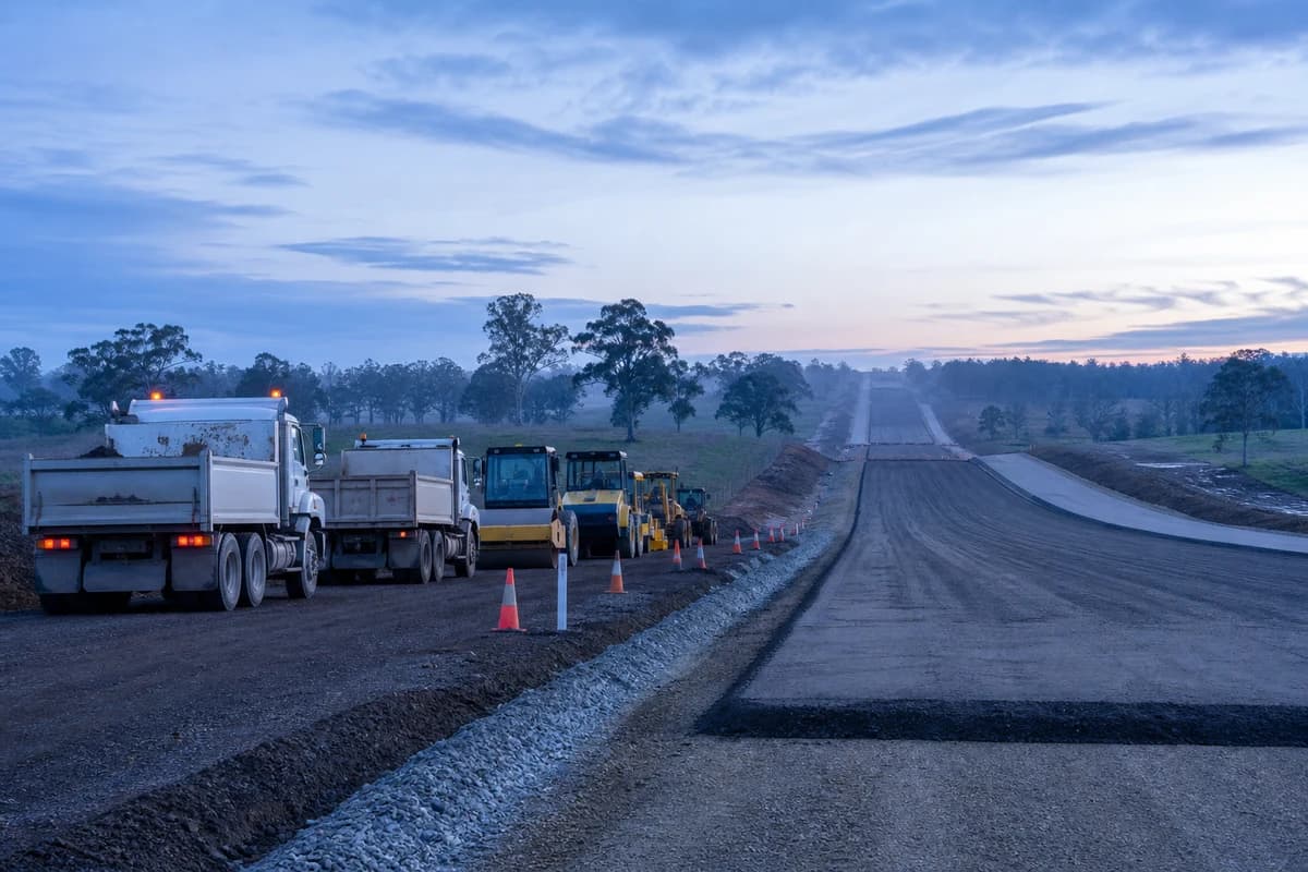 Access road construction NSW plant fleet beside unfinished pavement layers in cool morning light
