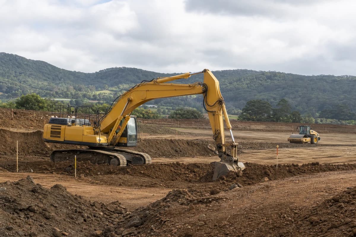 Earthworks Illawarra site with excavator grading a construction pad near escarpment foothills