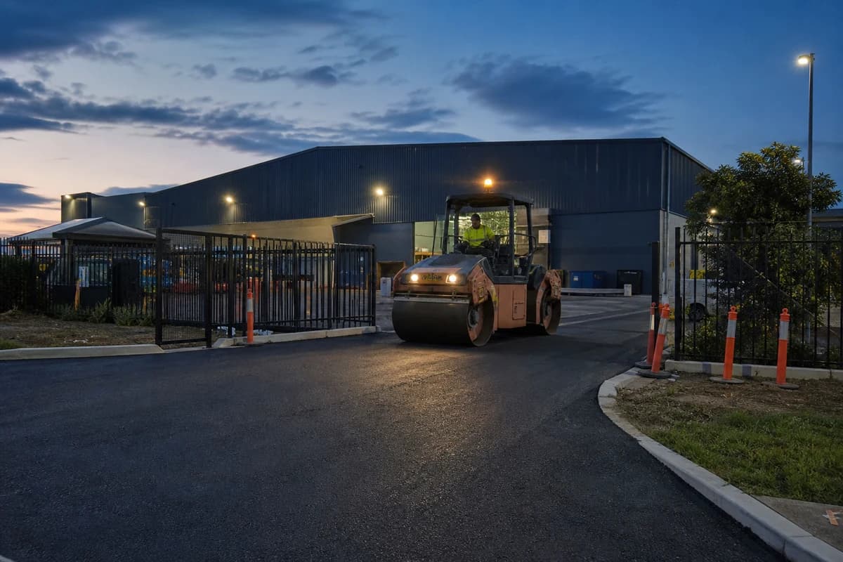 Roadworks Wollongong industrial truck-gate pavement with roller at dusk outside warehouse lights