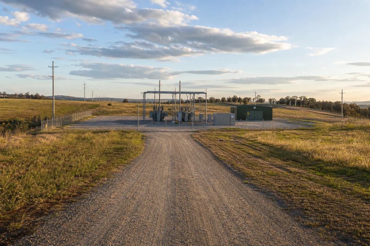 Renewable access road leading to a fenced substation compound pad across open NSW renewable corridor at late afternoon