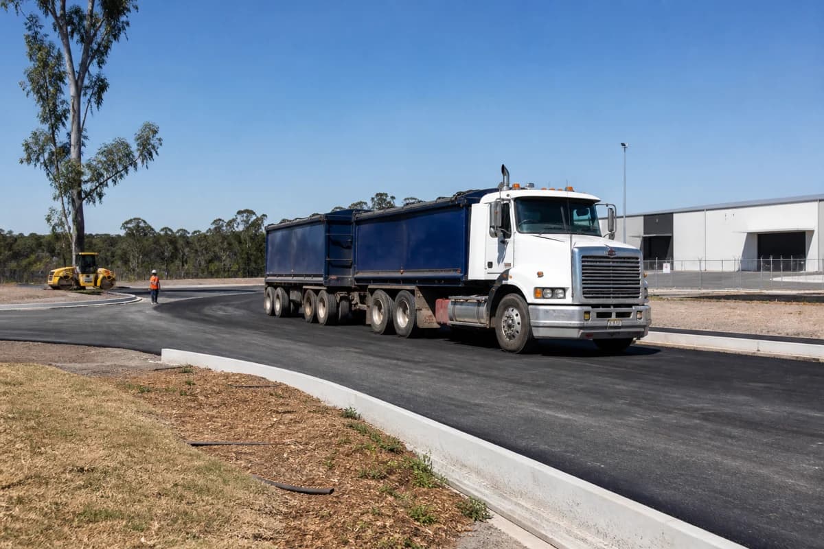 Industrial pavement works NSW heavy-vehicle turning on a newly compacted estate access road beside warehouse sheds in New South Wales, Australia