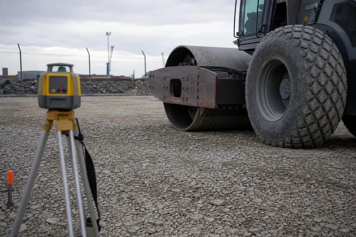 Earthworks Port Kembla hardstand pad with roller compaction and laser level check beside industrial fencing