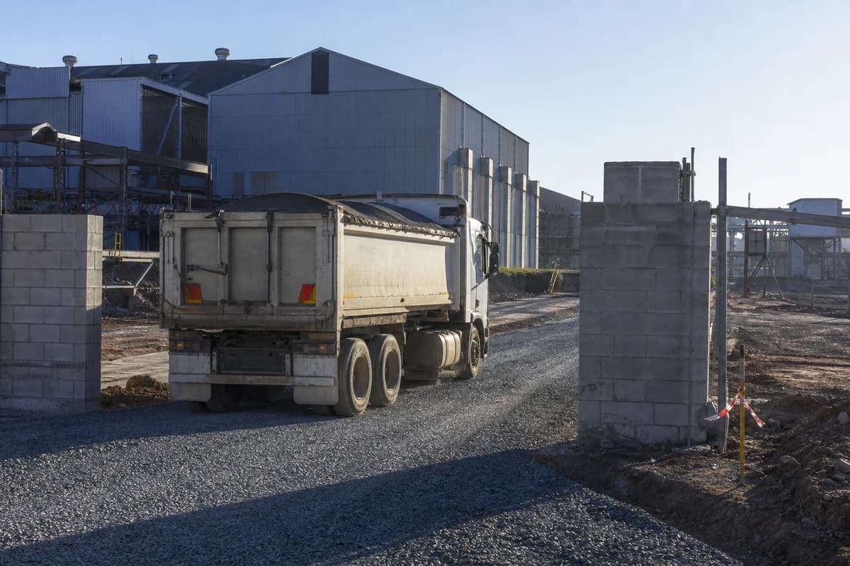 Roadworks Port Kembla access strip with fresh basecourse and a tipper leaving a hardstand gate in clear morning light