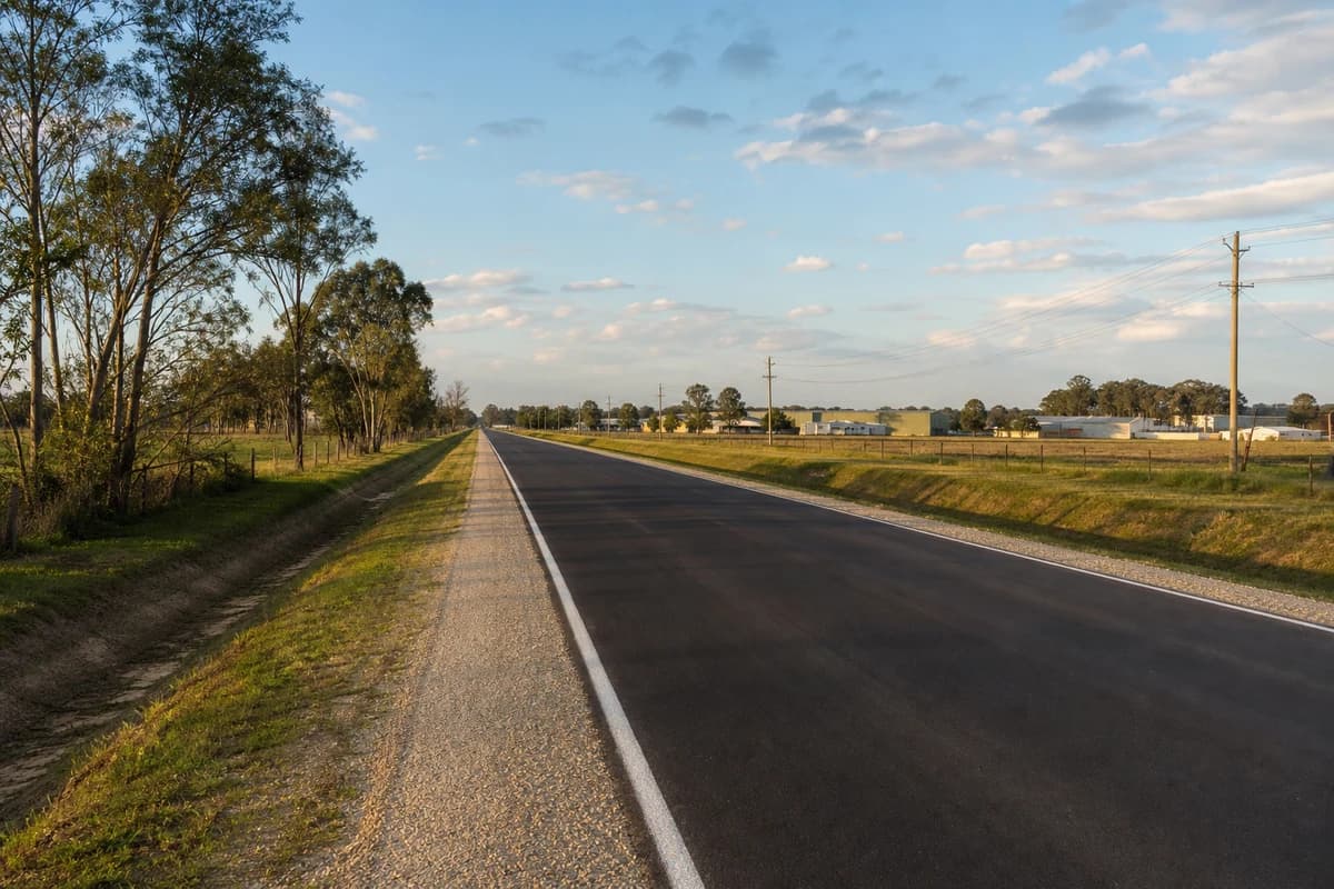 Rehabilitated NSW industrial access road with restored shoulders and clear table drains under late afternoon light