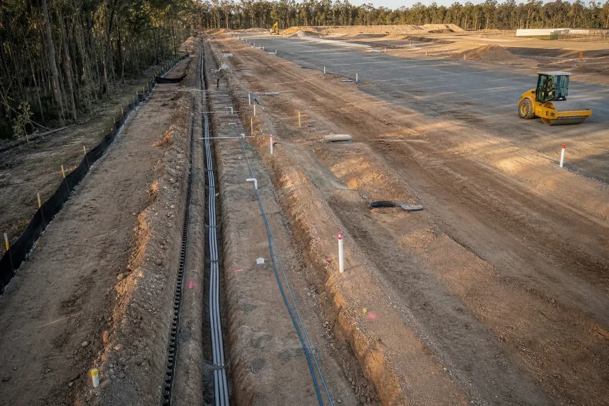 Industrial service corridor trench runs aligned for future pavement zones in New South Wales with construction vehicles and erosion controls