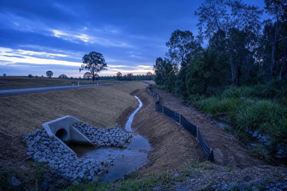 Civil drainage contractor outlet and roadside swale discharging to a vegetated channel at dusk in NSW