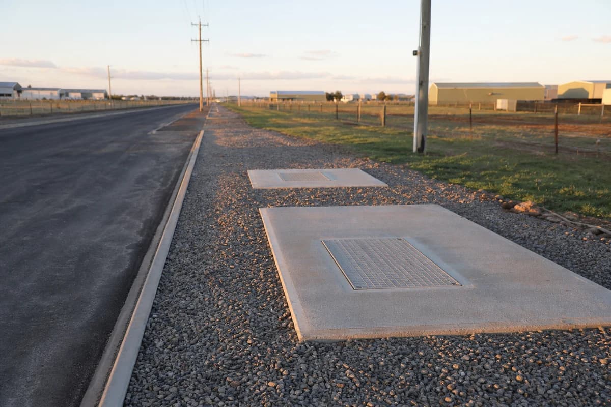 Reinstated utility corridor beside an NSW industrial access road with pit lids and fresh gravel verge at late afternoon
