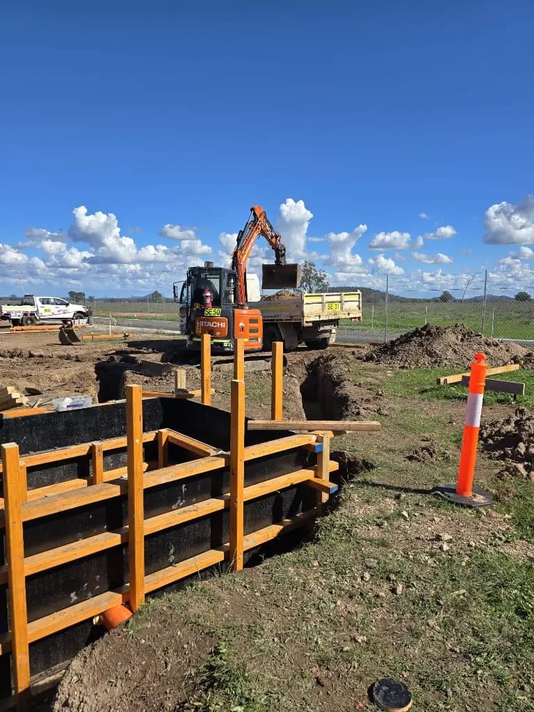 Excavator working beside structural civil works on a renewable energy site.