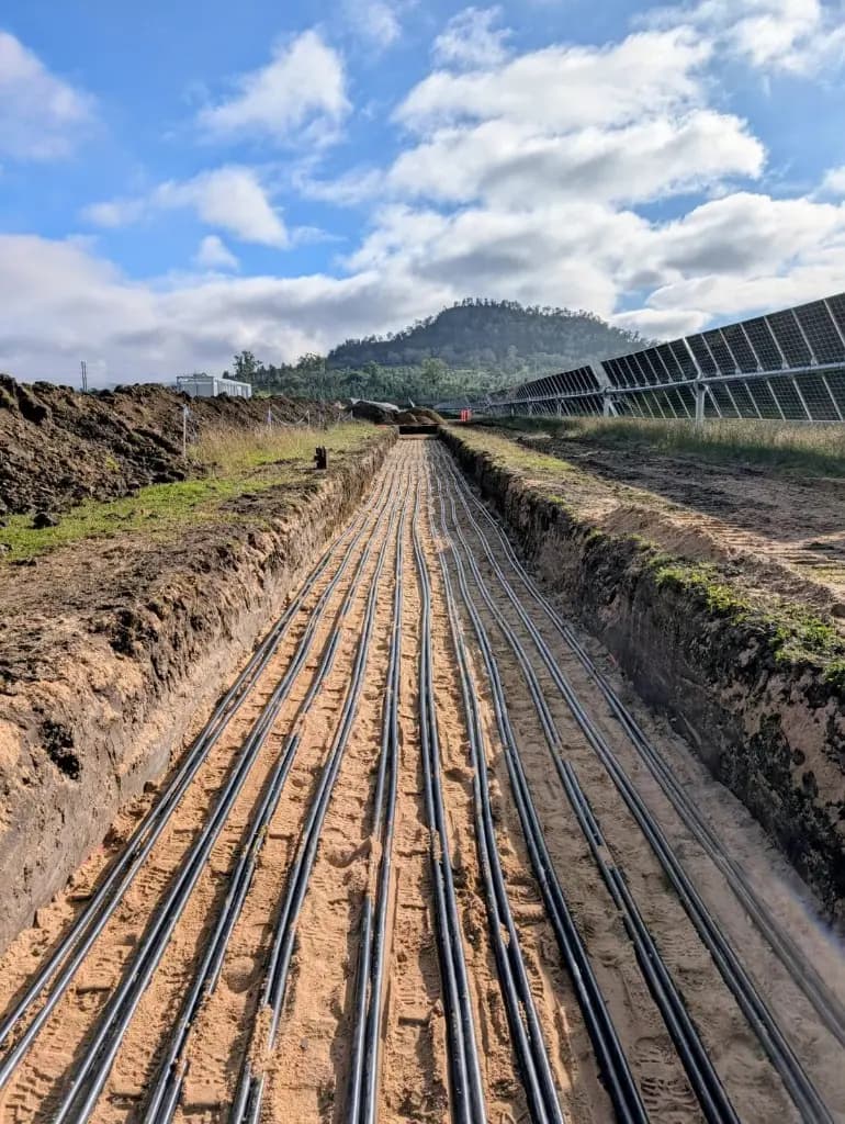 Renewable energy cable trench with conduits running beside solar panel arrays.