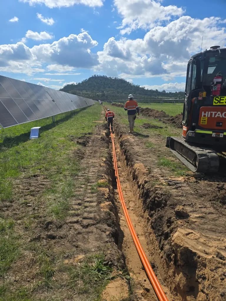 Excavator forming cable trenches across a solar array civil workfront.
